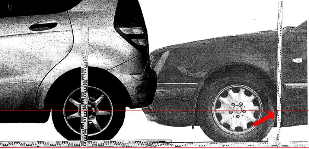 Zwei Fahrzeuge stehen sich Stoßstange an Stoßstange gegenüber, umgeben von Markierungen auf dem Boden. Ein Sachverständiger mit Klemmbrett begutachtet die Anstoßstellen beider Fahrzeuge. Die Szene zeigt eine realitätsnahe Fahrzeuggegenüberstellung zur Rekonstruktion eines Unfalls. Im Hintergrund erkennt man Messinstrumente und Absperrbänder.